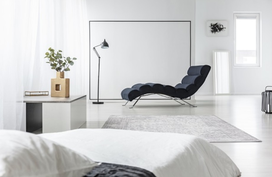 Lamp next to black chaise lounge in open space interior with white bed and plant on a table